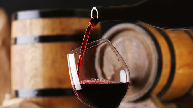 Pouring red wine from bottle into glass with wooden wine casks o